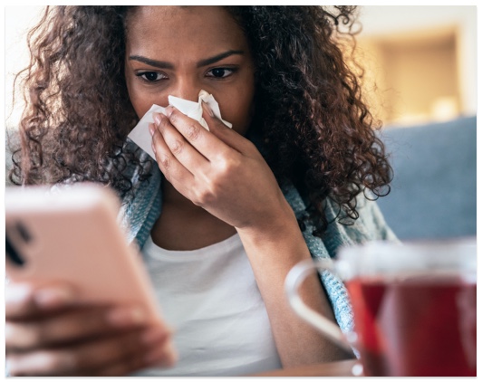 Young, African American woman with a cold using her phone.